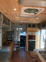 RV rental camper interior: cozy mobile kitchen, bed, fridge, microwave, and wood-paneled ceiling.