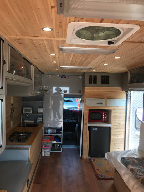 RV rental camper interior: cozy mobile kitchen, bed, fridge, microwave, and wood-paneled ceiling.