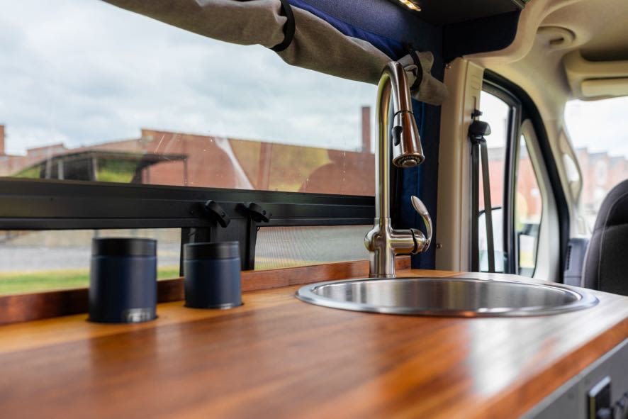 Inside an RV rental: a modern kitchen area with a sink, faucet, and rich wooden counter, ready for adventures.