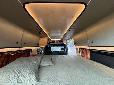 Inside a spacious rv rental: comfortable bed, sleek ceiling lighting, and front cab view of nature.