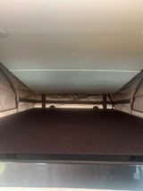 Inside an RV rental pop-top camper: a view of the elevated sleeping area with its bed, fabric walls, and ceiling.