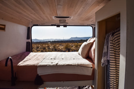 Inside a comfy RV rental: bed, simple kitchenette, closet, and scenic desert mountain views from the open back.