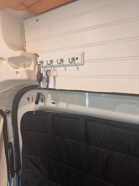 RV rental interior: white beadboard wall with a key rack holding keys, over a black padded door panel.