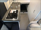 Modern RV rental interior with compact kitchen (sink, stove, fridge), storage, and bed area for comfortable travel.
