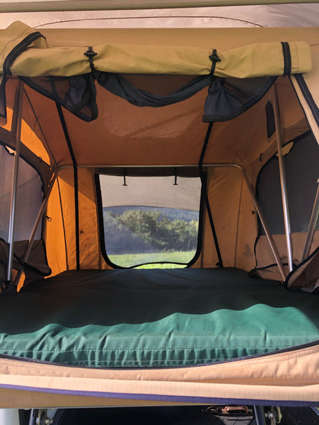 Interior of a comfortable rooftop tent, perfect for an RV rental adventure, with a green mattress and nature view.