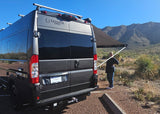Relaxing with an RV rental: a grey camper van with an extended awning, parked in a scenic desert mountain setting.