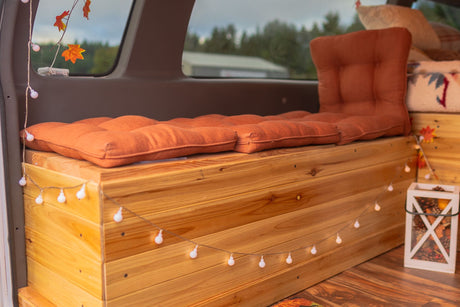 Cozy RV rental interior with a wooden bench, orange cushions, and fall decor, illuminated by string lights.