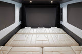 Luxury RV rental interior featuring a spacious, cream-colored modular bed/seating area, with a large screen overhead.