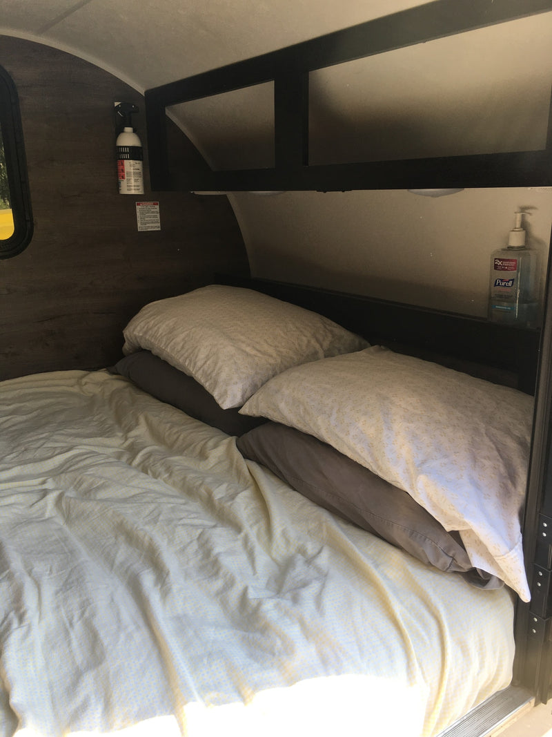 Cozy RV rental sleeping area: bed with light sheets & pillows, overhead shelving, fire extinguisher, and hand sanitizer. — photo 14