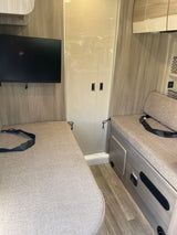 Interior of an RV rental: two cushioned benches with seatbelts, a wall-mounted TV, and a central cabinet.