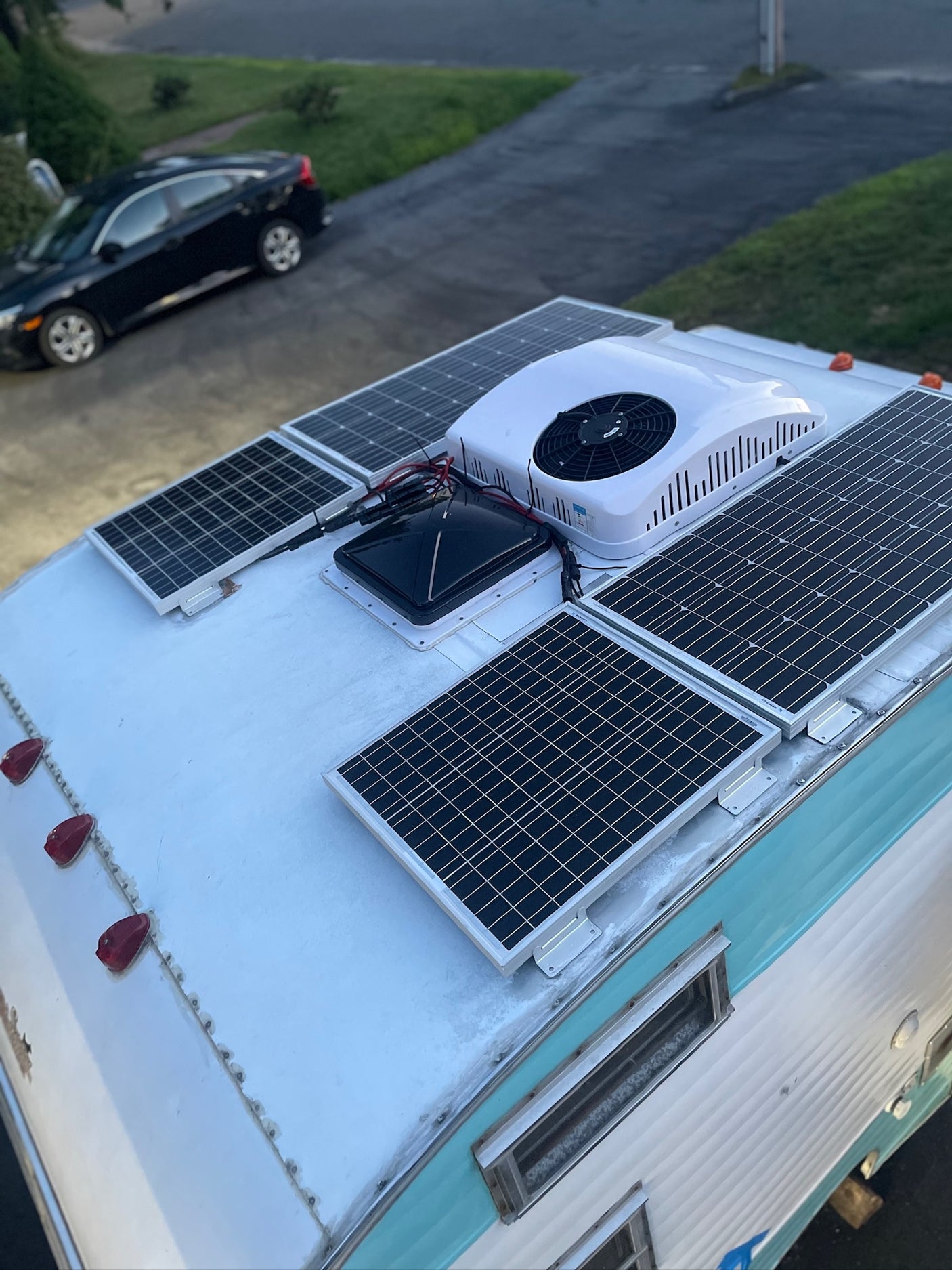 Top-down view of an RV rental roof with solar panels, a rooftop AC unit, and a vent fan for off-grid living.