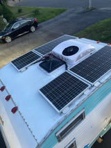 Top-down view of an RV rental roof with solar panels, a rooftop AC unit, and a vent fan for off-grid living.