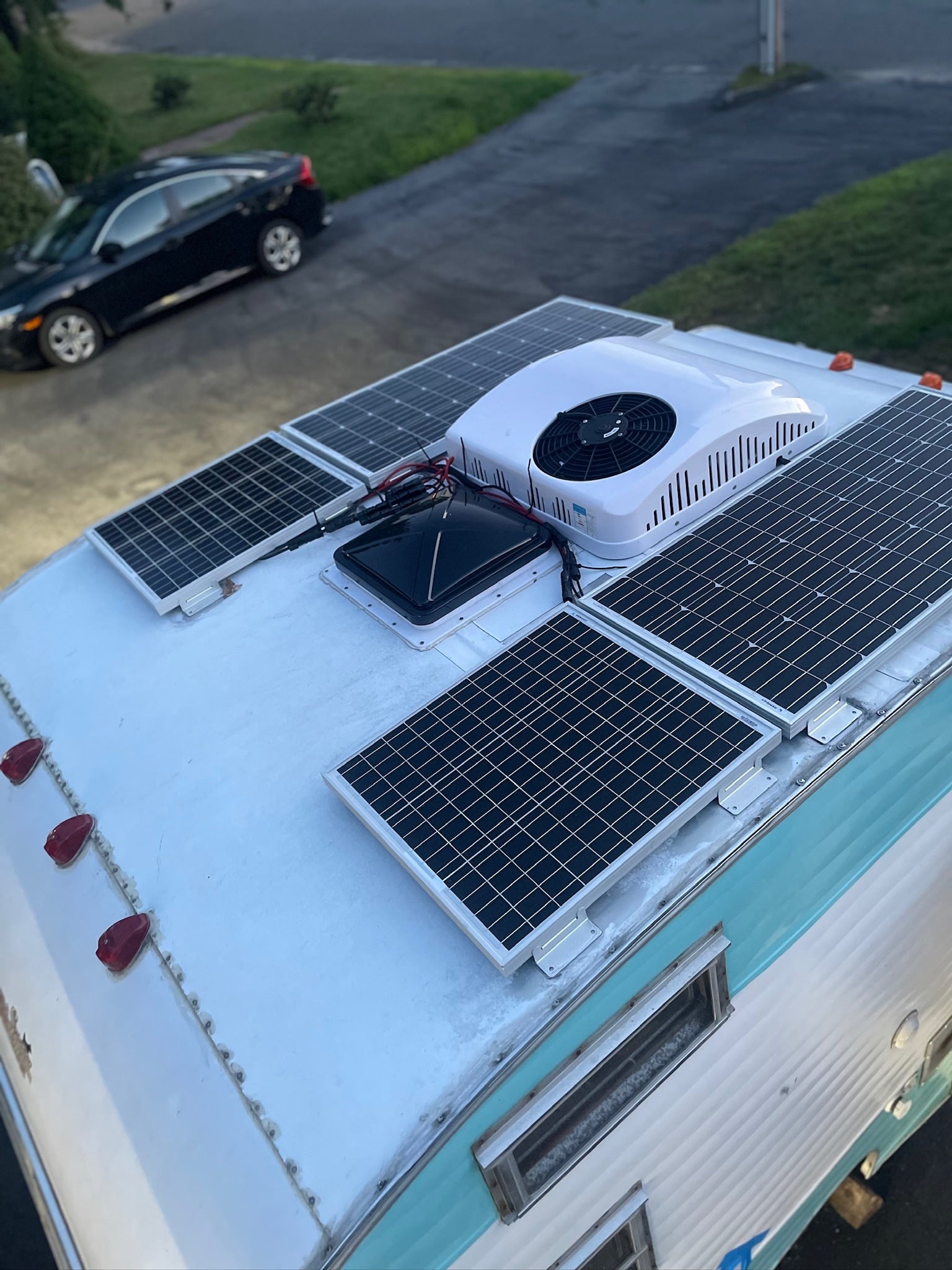 Top-down view of an RV rental roof with solar panels, a rooftop AC unit, and a vent fan for off-grid living.