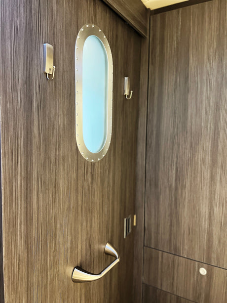This modern RV rental interior features a unique porthole window, sleek handle, and hooks on a dark wood-textured wall.