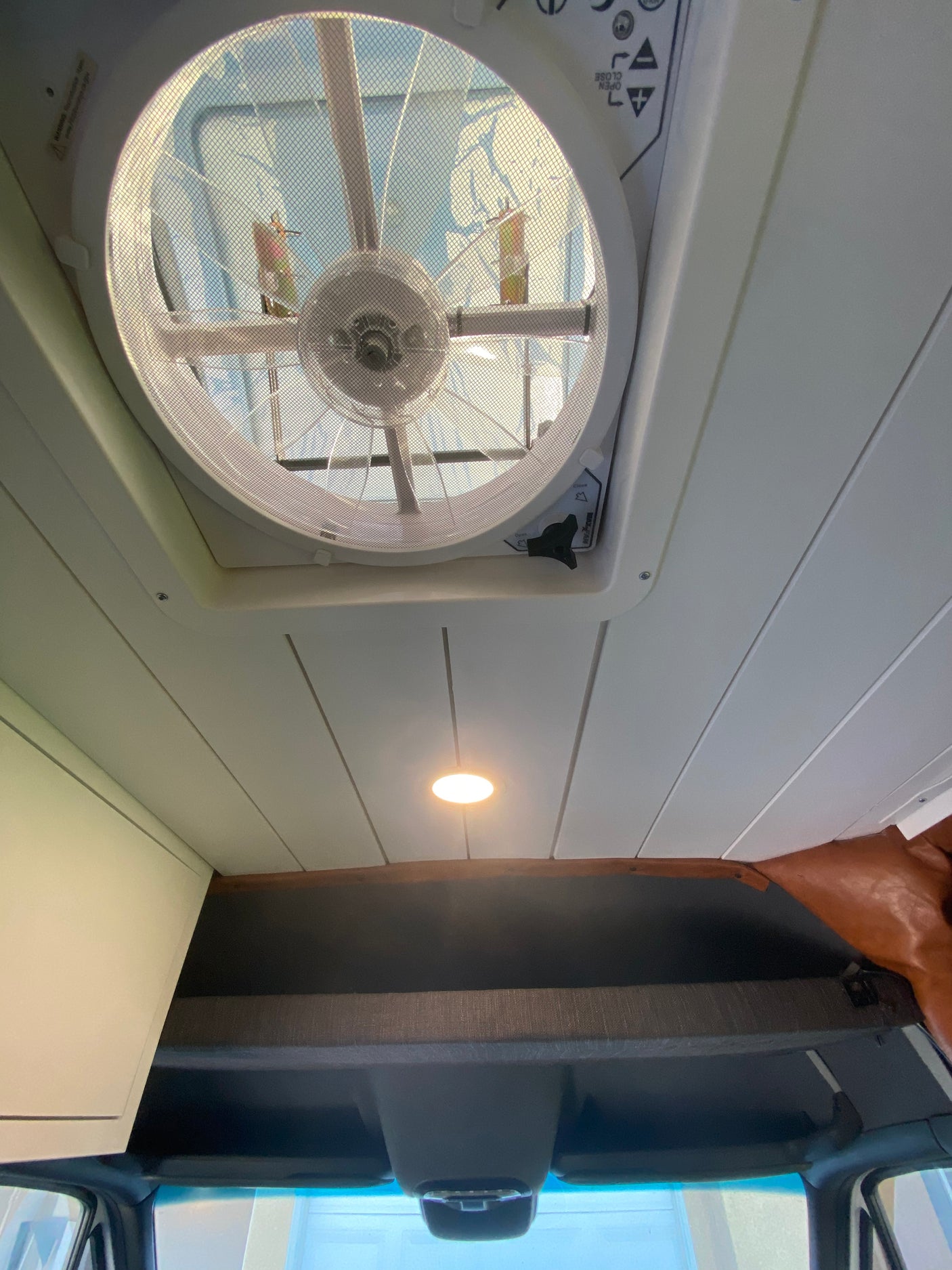 Looking up at the modern interior of an rv rental: a large ceiling fan with mesh, recessed LED light, & white paneled ceiling.
