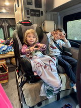 Two kids making fun poses in their car seats during an RV rental trip, ready for adventure.