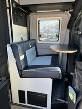 Interior view of an RV rental, featuring a gray dinette bench, table, and a wall-mounted control panel.