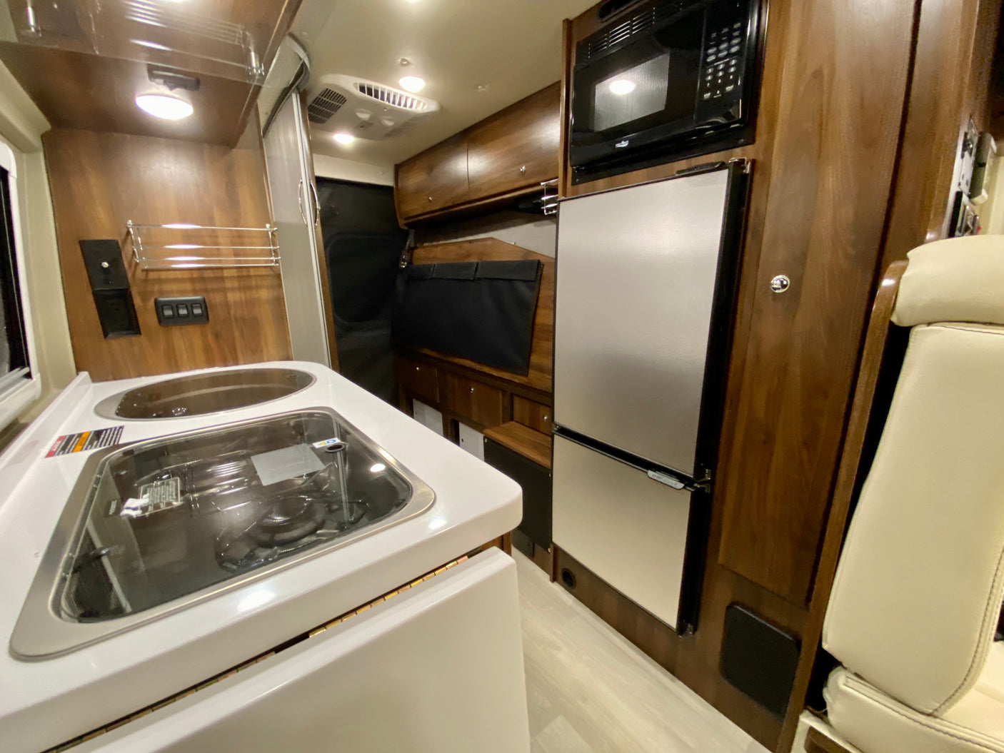 Modern RV rental interior: well-equipped kitchen with sink, stovetop, fridge, and microwave, perfect for road trips.