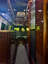 Experience an upscale RV rental interior featuring glossy dark wood, bright recessed lighting, a modern Dometic AC, and comfortable rear seating.