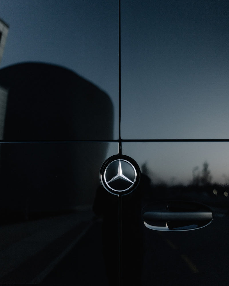 A dark Mercedes-Benz rv rental's side, showing its iconic star logo and door handle. Reflections add detail to the sleek panel. — photo 9