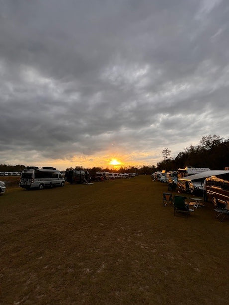 Serene sunset over a large RV gathering, showcasing various campervans and motorhomes, perfect for an RV rental trip.