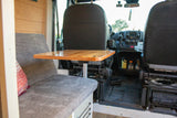 RV rental interior features a shiny wooden table, comfy grey seating, and front cab view. Ideal setup for travel & remote work.