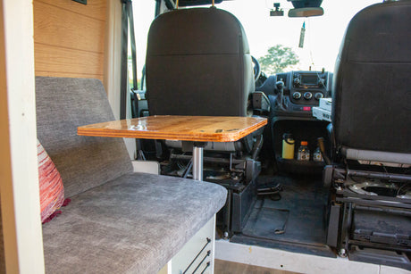 RV rental interior features a shiny wooden table, comfy grey seating, and front cab view. Ideal setup for travel & remote work.