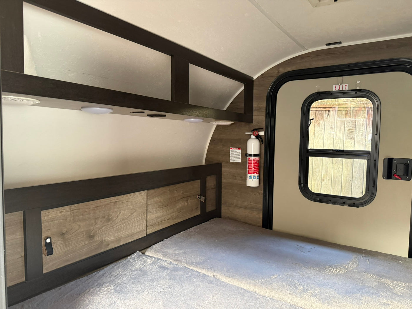 RV rental bedroom area showing a bed, wood-paneled walls, overhead storage, exit door, and a fire extinguisher. — photo 6