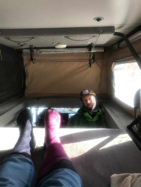Feet up, relaxing inside a cozy rv rental, looking at a man in a hat and green jacket.