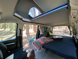 Cozy RV rental interior with bed, guitar, and open pop-top roof. Perfect for van life camping adventures in nature.