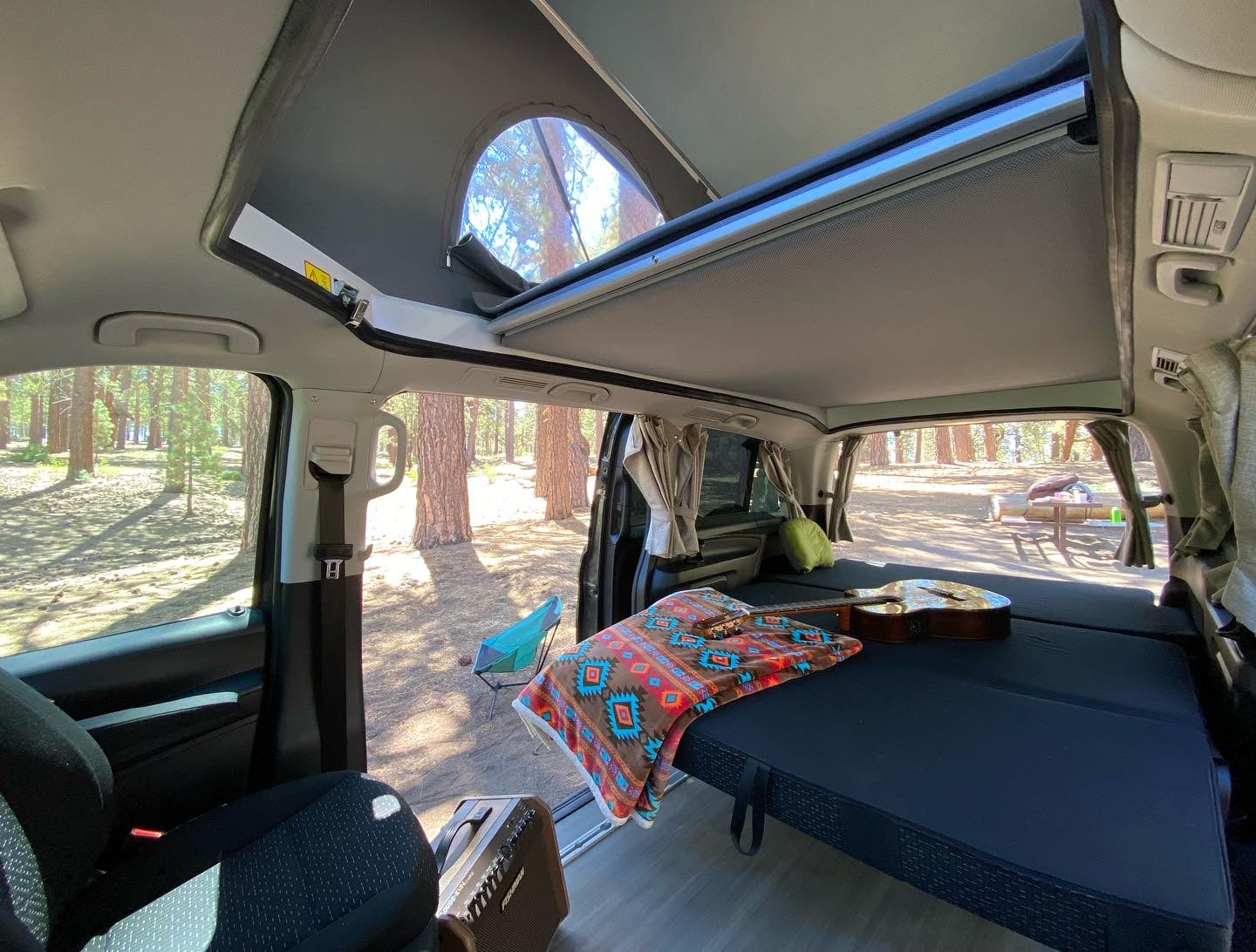 Cozy RV rental interior with bed, guitar, and open pop-top roof. Perfect for van life camping adventures in nature.