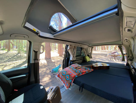 Cozy RV rental interior with bed, guitar, and open pop-top roof. Perfect for van life camping adventures in nature.