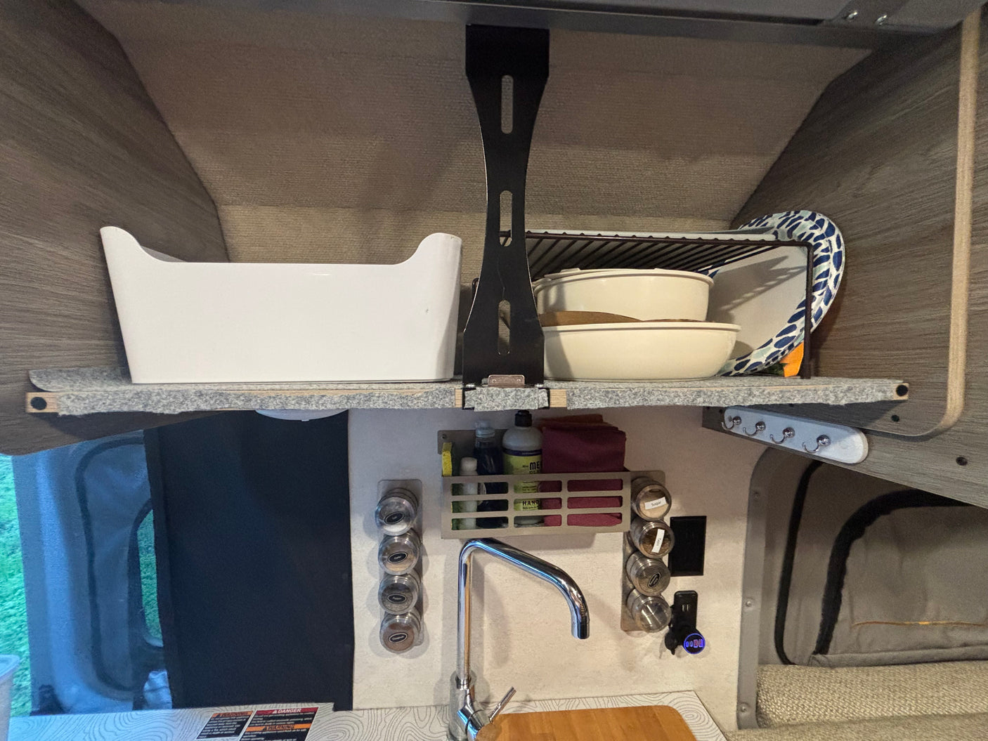 Organized RV rental kitchen area with shelves, sink, spice rack, and storage caddy, maximizing space for travelers.