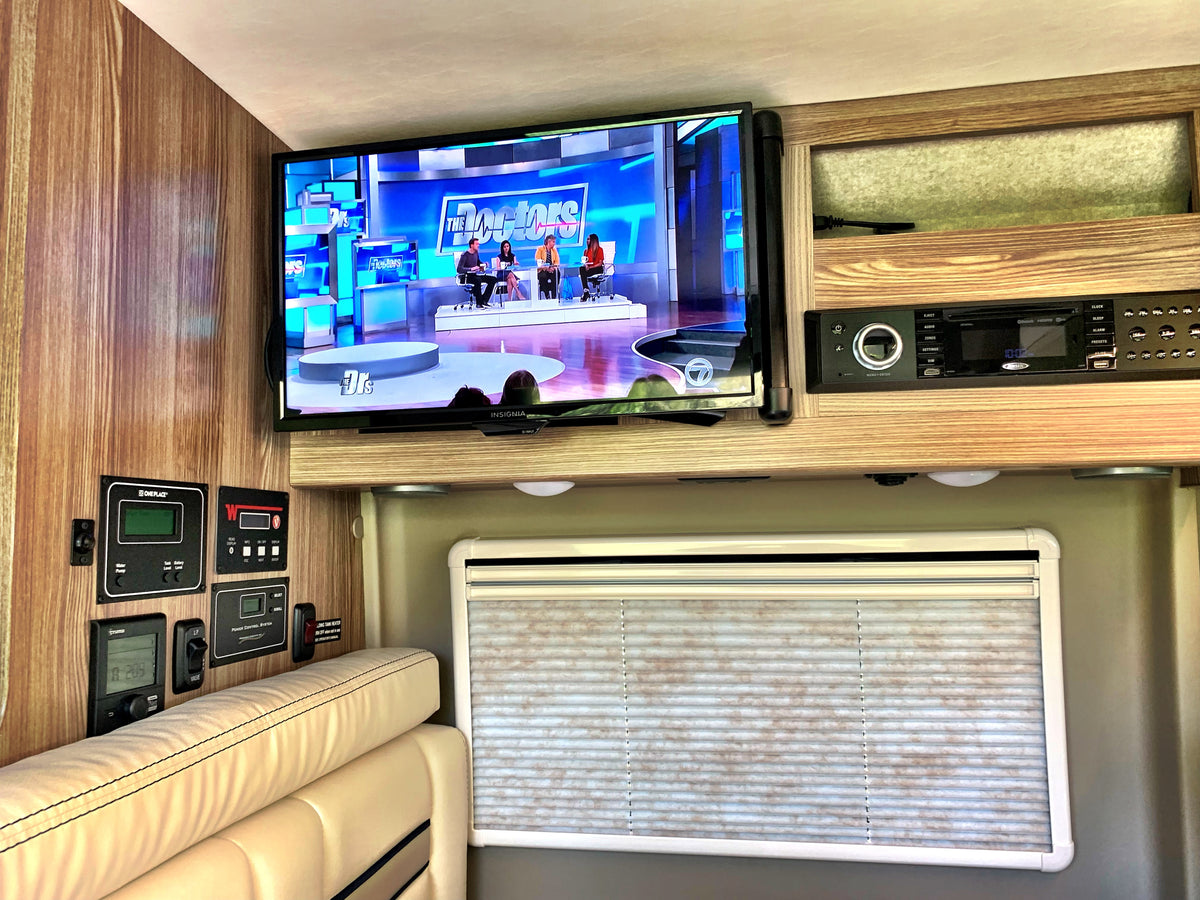 RV rental: Interior view with TV playing "The Doctors," control panels, and entertainment system above seating and a window. — photo 4