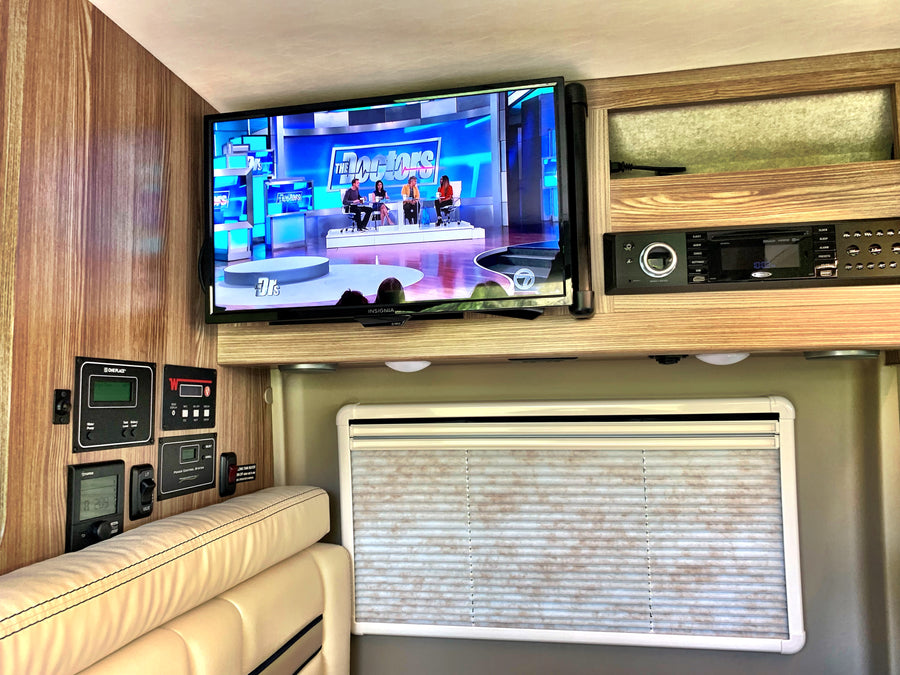 RV rental: Interior view with TV playing "The Doctors," control panels, and entertainment system above seating and a window.