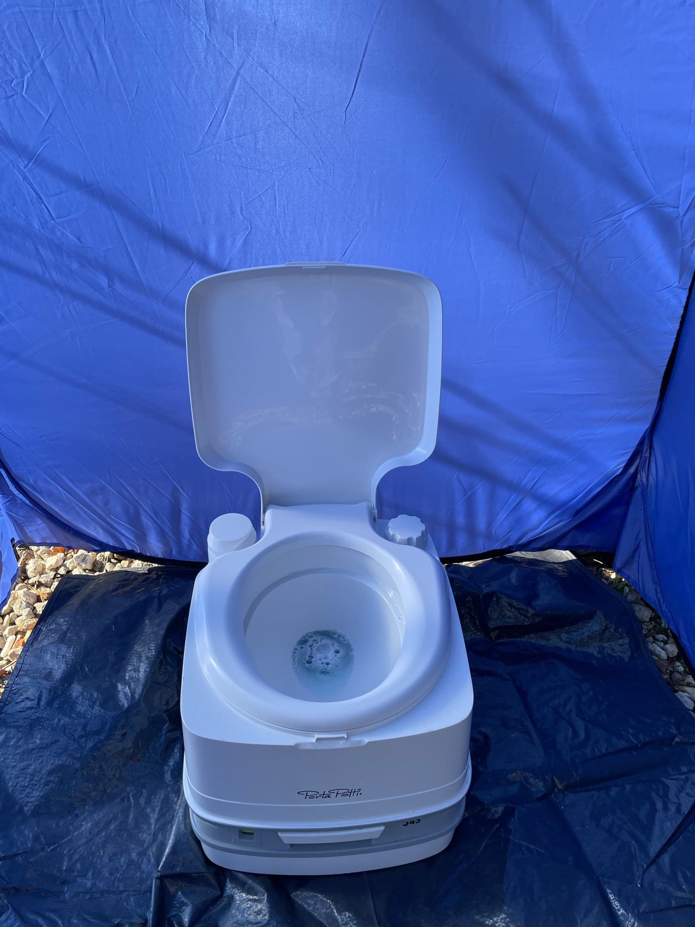 Portable Porta Potti toilet inside a blue privacy tent on a tarp, ideal for rv rental or camping sanitation.