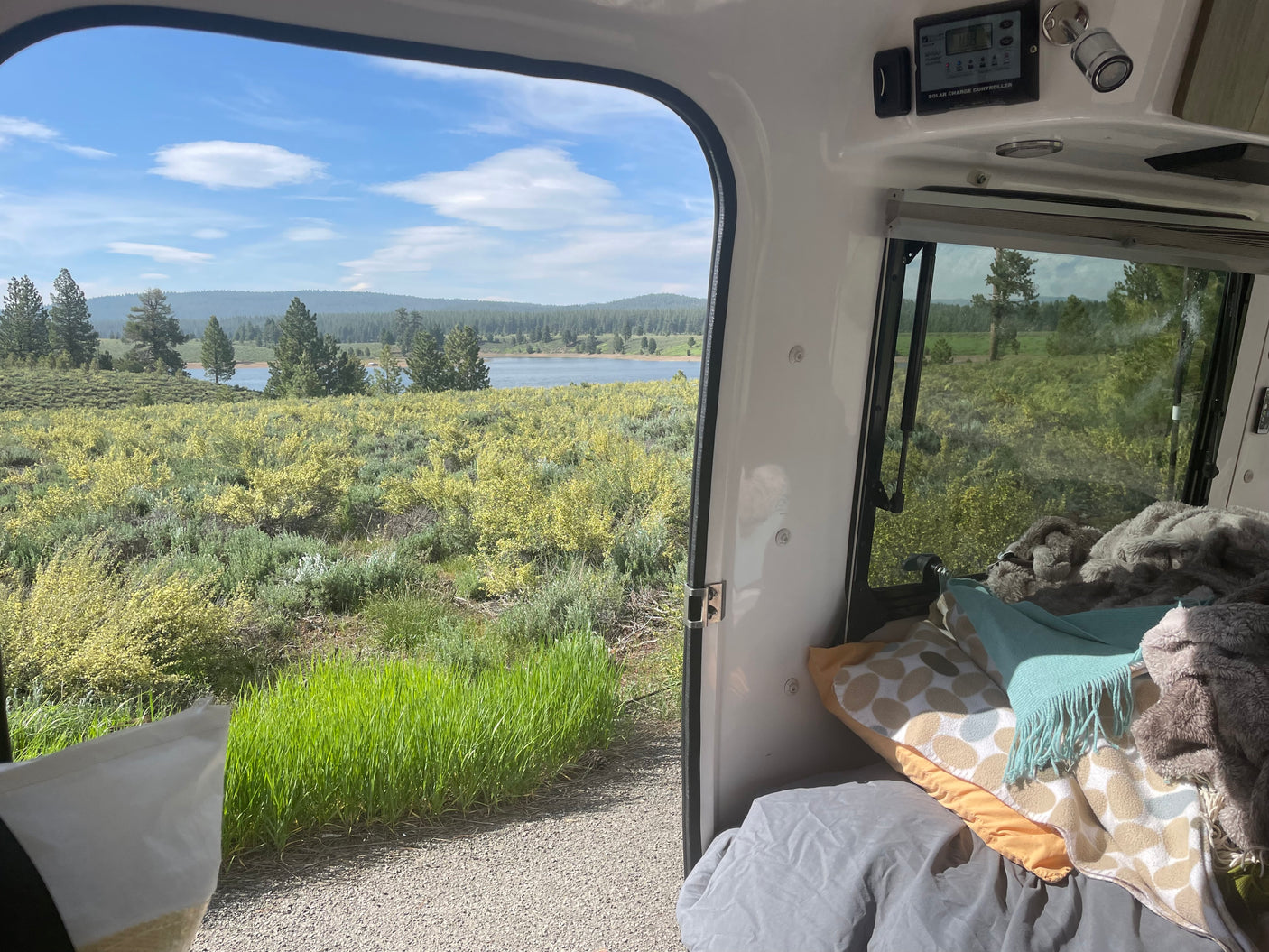 Enjoying a scenic lake view from a comfy rv rental, featuring a solar charge controller and cozy bedding inside.