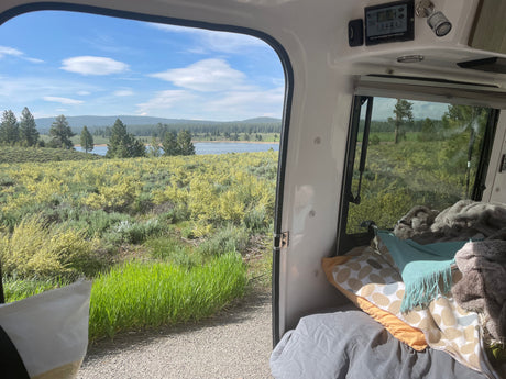 Enjoying a scenic lake view from a comfy rv rental, featuring a solar charge controller and cozy bedding inside.