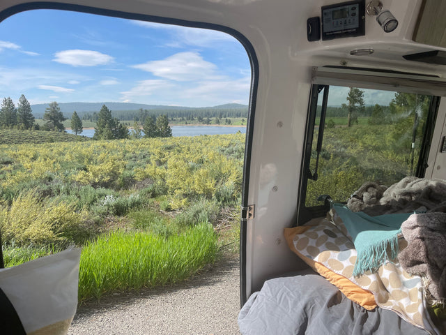 Enjoying a scenic lake view from a comfy rv rental, featuring a solar charge controller and cozy bedding inside.