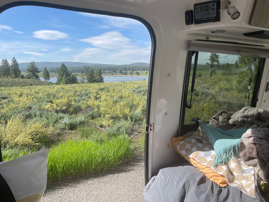 Enjoying a scenic lake view from a comfy rv rental, featuring a solar charge controller and cozy bedding inside.
