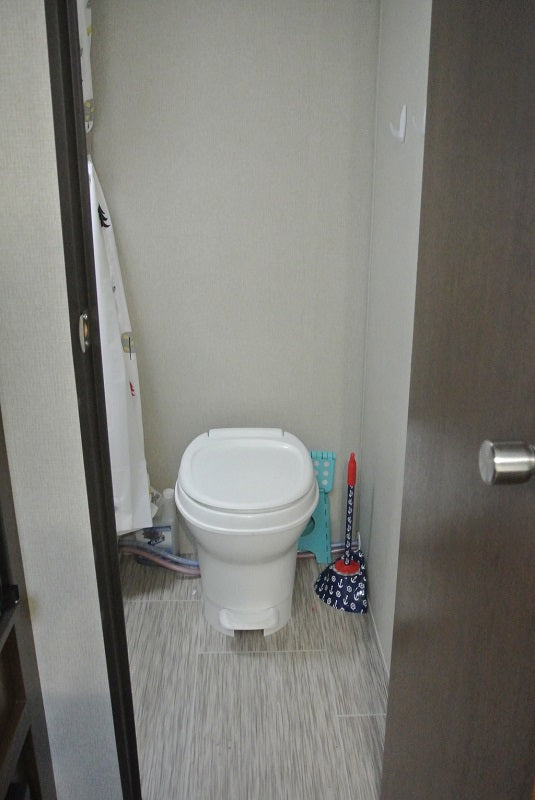 Compact RV rental bathroom with a white toilet, shower curtain, and light gray striped floor.