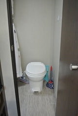 Compact RV rental bathroom with a white toilet, shower curtain, and light gray striped floor.