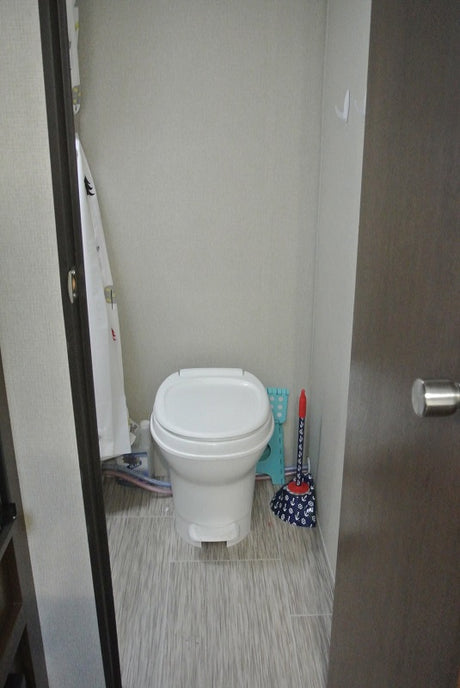 Compact RV rental bathroom with a white toilet, shower curtain, and light gray striped floor.