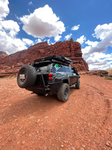 Rugged black SUV, an overlanding RV rental with rooftop tent, navigates red rock terrain. Ready for your desert adventure!