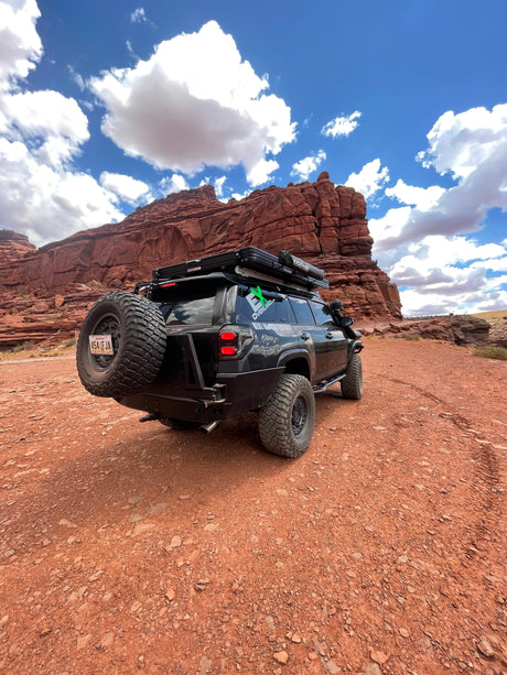 Rugged black SUV, an overlanding RV rental with rooftop tent, navigates red rock terrain. Ready for your desert adventure!
