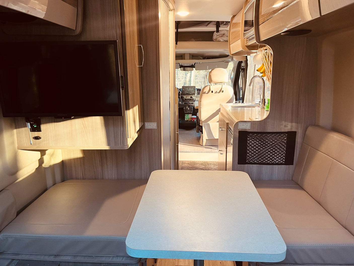 Bright RV rental interior: dinette, TV, kitchen, and driver's cabin view. Ideal for a comfortable camper van trip.