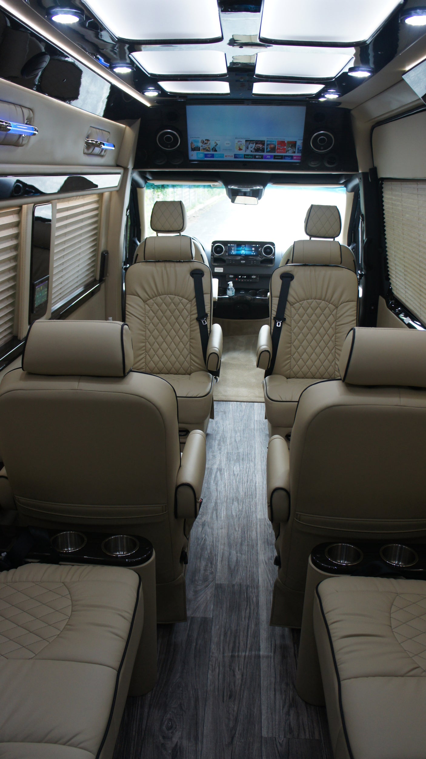 Step inside this luxury RV rental: a spacious custom van with plush beige leather seats, a large TV, and ambient lighting.