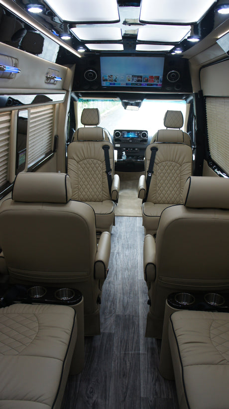 Step inside this luxury RV rental: a spacious custom van with plush beige leather seats, a large TV, and ambient lighting.