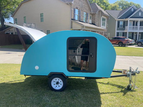 Vibrant teal teardrop trailer for rv rental parked on grass. Ideal for camping & travel, a compact tiny camper.