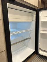 This clean, empty rv rental refrigerator is ready for use. Its interior shows shelves and a small freezer, a key kitchen appliance.